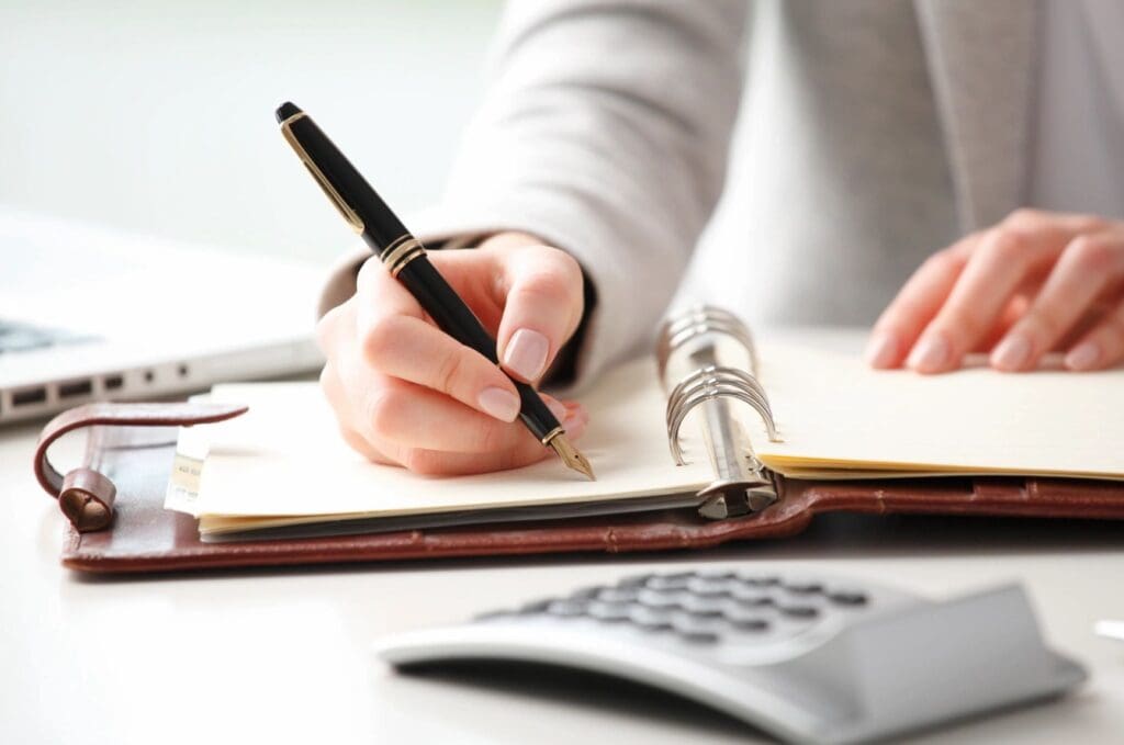 A person writing in a notebook with a pen.