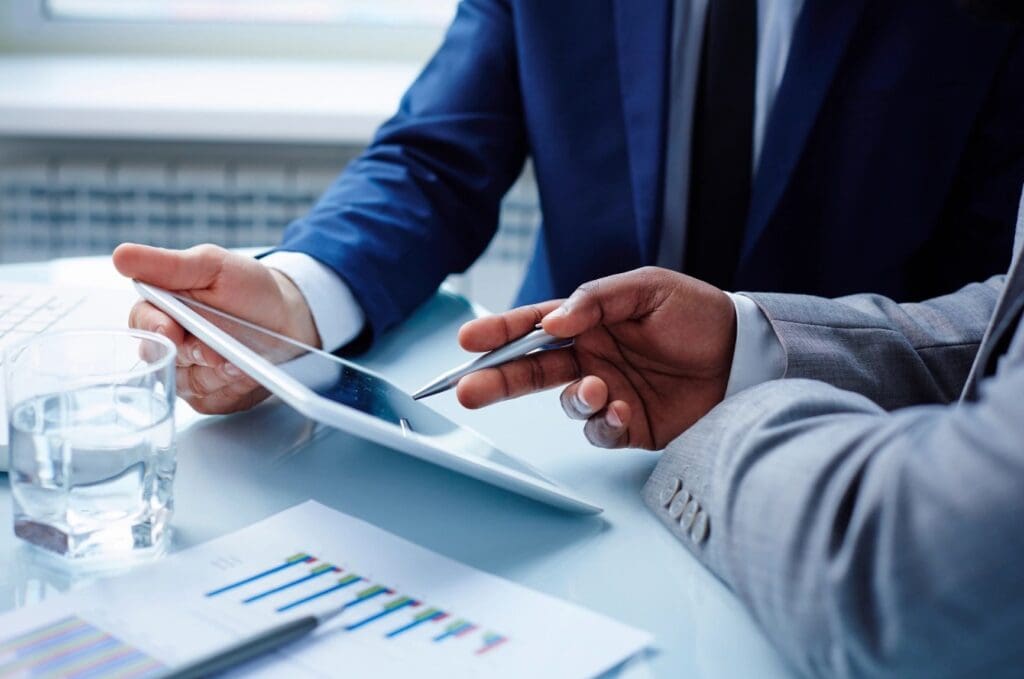 Two people sitting at a table with papers and a tablet.