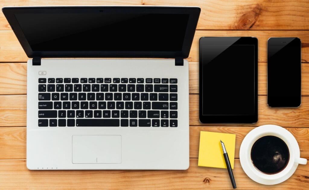 A laptop and tablet sitting on top of a wooden table.